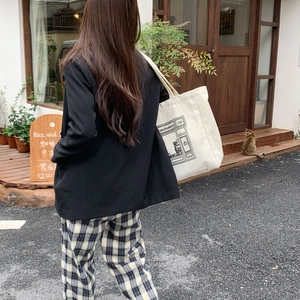 Outdoor street view of a woman carrying a white printed canvas tote bag from behind
