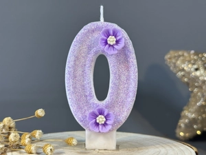Detail of purple number 0 birthday candle with glitter and resin flower decorations