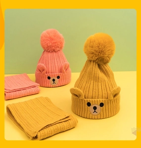 Detail of pink and yellow knitted baby hat with bear ears and faux fur pom-pom