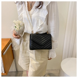 Detail of black V-quilted crossbody bag with elegant pearl strap on female model