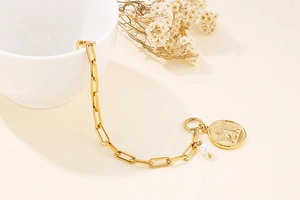Detail of gold chain bracelet with angel coin pendant and small pearl charm decoration