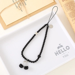 Black beaded phone strap with cherry pendant and metal charms on a vintage backdrop