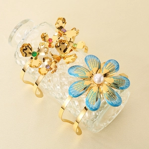 Detail of gold floral bangles with blue enamel and pearls on a glass bottle