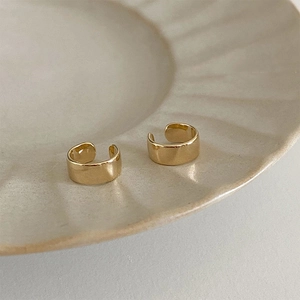 Detail of wide C-shaped gold ear cuffs on a textured cream ceramic plate