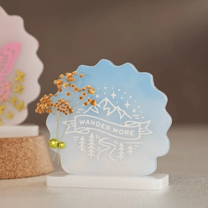 Detail view of acrylic mountain ornament with Wander More text and dried flower decor