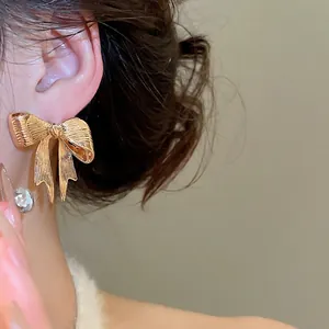 Orecchini a fiocco in metallo dorato lucido con texture spazzolata su modella