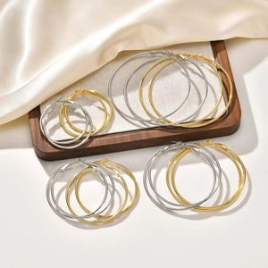 Detail of gold and silver large stainless steel hoop earrings set on beige silk
