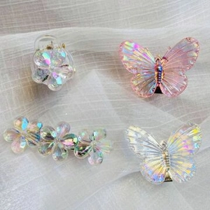 Detail of holographic butterfly and flower hair clips set on white fabric texture