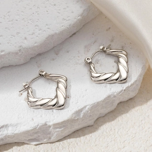 Macro detail of silver twisted square hoop earrings on stone and silk background