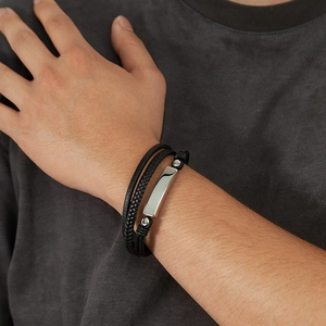 Detail of a men's multilayered black braided leather bracelet with silver metal plate