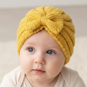 Close-up of ginger yellow baby knit hat with large bow and soft ribbed texture detail