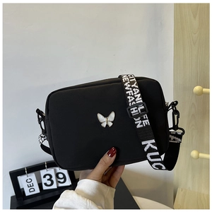 Close-up of black nylon crossbody bag with butterfly badge and lettered wide strap