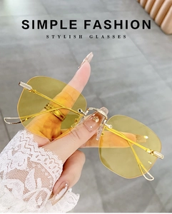 Detail of yellow rimless sunglasses with gold metal temples held by hand