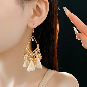 Detailed side view of model wearing golden leaf earrings with beige tassels and oil drip finish