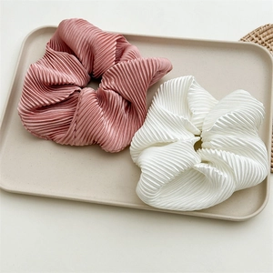 Close-up of pink and white ruffled satin hair scrunchies on a minimalist tray