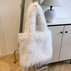 Detailed view of a white fluffy faux fur tote bag with fringe hanging on a metal hanger