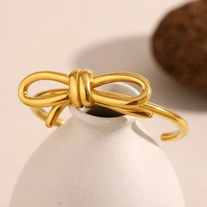 Detailed close-up of a 18K gold-plated stainless steel bow knot open bangle on a vase