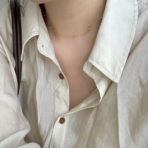 Close-up of a minimalist gold beaded chain necklace worn on a model's neck