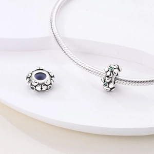 Macro shot of silver heart-shaped relief charm with green gemstone on snake chain