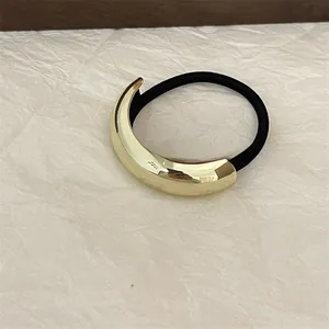 Macro detail of high-elastic black hair tie with curved gold metal clasp on white paper