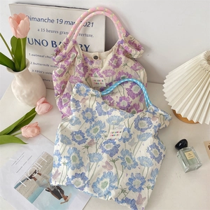 Detail of floral canvas tote bags with woven rope handles and brand label on desk