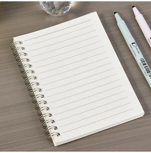 Detail view of white spiral notebook with silver metal coil on grey wood background