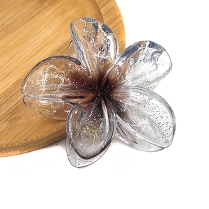 Detailed top view of a translucent taupe plumeria flower hair claw with silver glitter