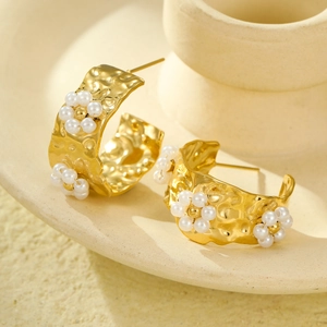 Close-up of gold-plated C-shape textured earrings with white pearl flower accents