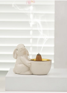 Detailed view of white ceramic rabbit incense burner with gold rim and smoking cone