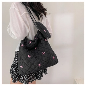 Detail of black quilted shoulder bag with pink bow embroidery and mini coin purse charm