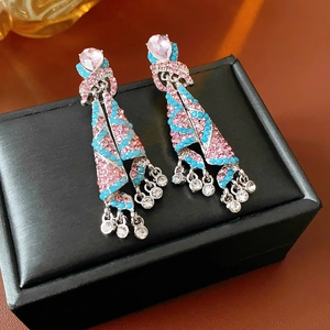 Vue macro des boucles d'oreilles à pompons en strass rose et bleu ciel sur boîte en cuir