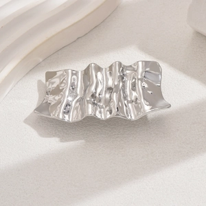 Irregular silver liquid metal hair clip with hammer texture on beige background