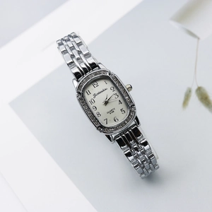 Detail of tonneau-shaped silver watch featuring rhinestones and Arabic numerals on white dial