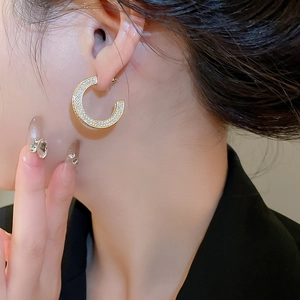 Close-up of elegant gold C-shaped earrings with shimmering zircons on model ear