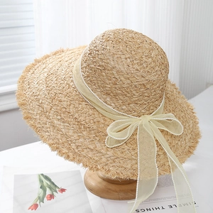 Détail d'un chapeau de soleil en raphia avec nœud en mousseline perlé et bord effiloché