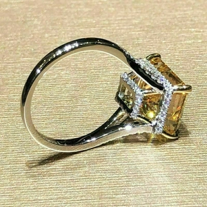 Close-up of radiant cut yellow gemstone ring with silver setting on gold background