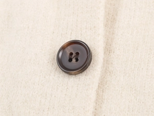 Gros plan sur la maille tricotée et le bouton en écaille d'un cardigan beige de qualité