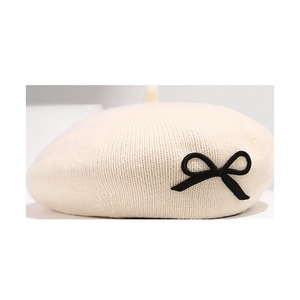 Béret tricoté blanc crème avec nœud noir décoratif et motif en maille verticale