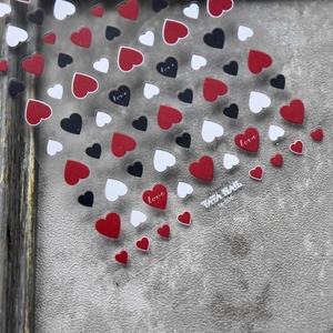 Detail view of heart nail art stickers with red and black motifs on textured background