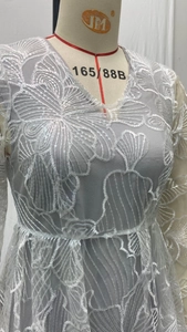 Detail of light gray lace dress featuring intricate white embroidery and sequins on mesh