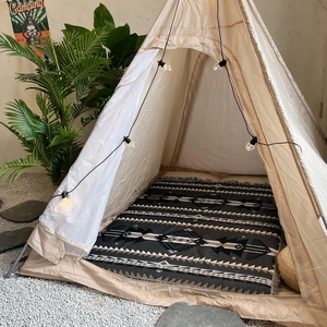 Detail view of a bohemian geometric rug with tassels inside a cozy beige play teepee tent