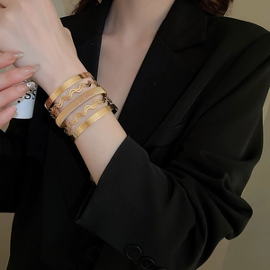 Close-up of stacked gold wave bracelets with textured and polished finish on wrist