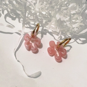 Détail de boucles d'oreilles fleur rose en résine avec créoles dorées 18K sur fond blanc