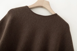 Detailansicht von Kragen und Schultertextur des braunen Strickponchos am Holzhaken
