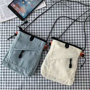 Detail of light blue and beige mini nylon crossbody bags with rope straps and orange accents