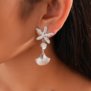 Macro shot of silver-colored starfish and seashell drop earrings on a model