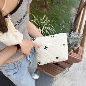 Close-up of white quilted cosmetic bag with black bow embroidery and brand label