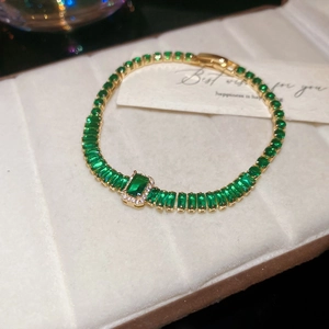 Macro detail of gold emerald bracelet with rectangular step-cut stones on white plush background