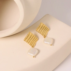 Baroque pearl drop earrings with wavy gold metal accents on a geometric display
