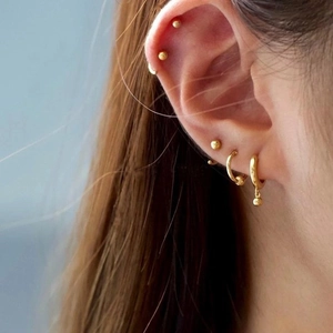 Primer plano de pendientes de bola y aros dorados minimalistas puestos en la oreja